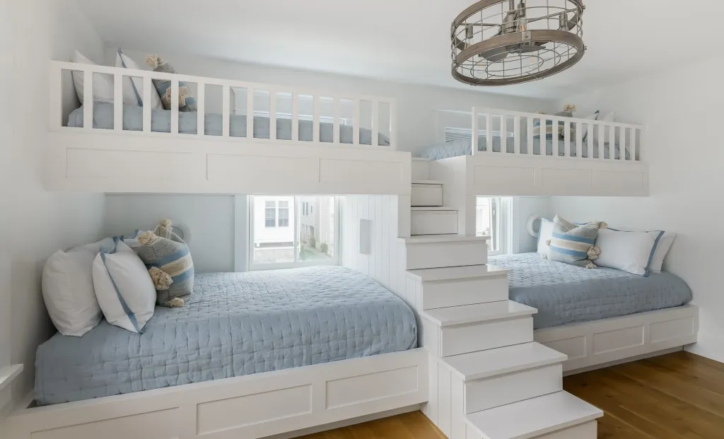 Nautical-themed bunk room featuring built-in bunk beds with blue bedding, integrated storage drawers, and a unique metal chandelier.