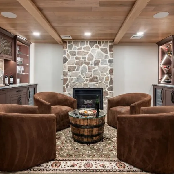 Cozy wine tasting room featuring custom cabinets, stone fireplace, and plush brown chairs.