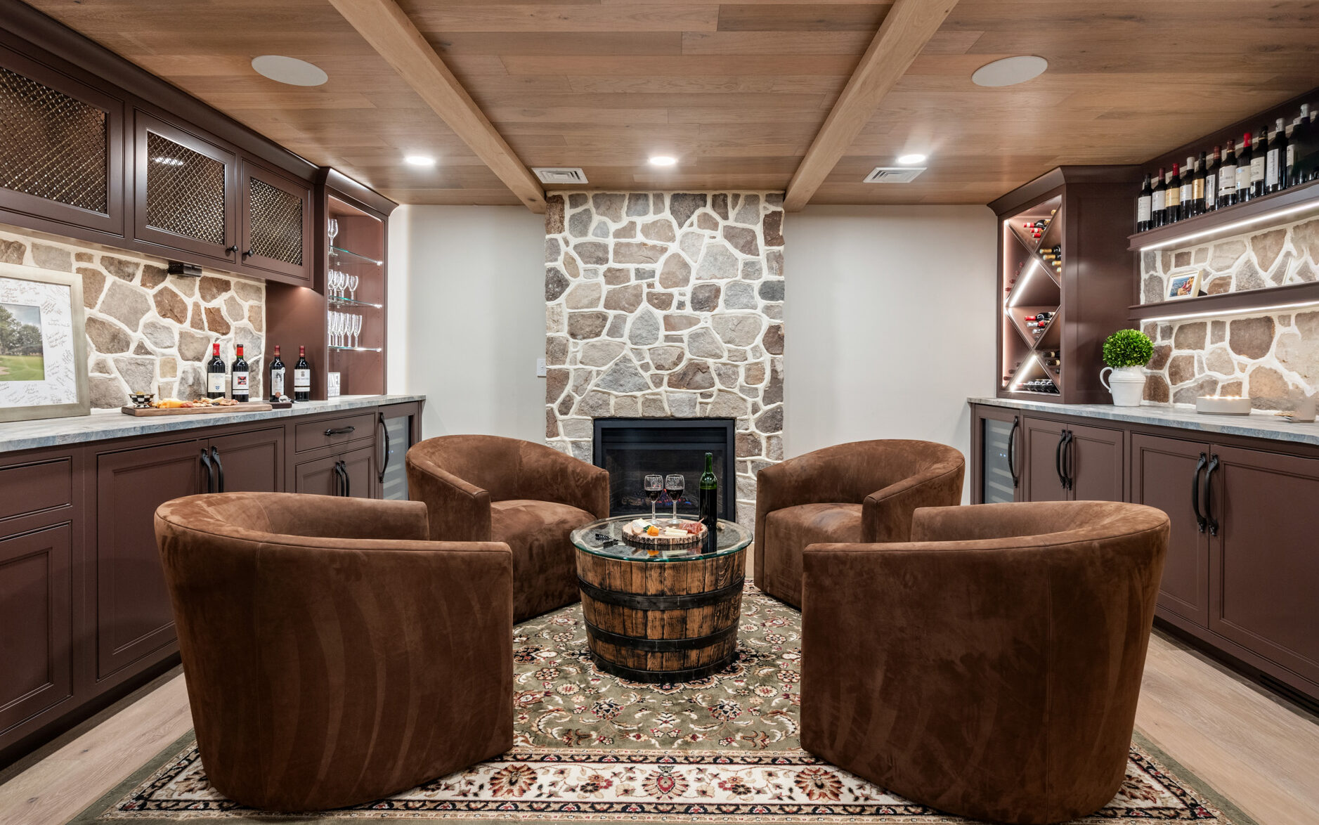 Cozy wine tasting room featuring custom cabinets, stone fireplace, and plush brown chairs.