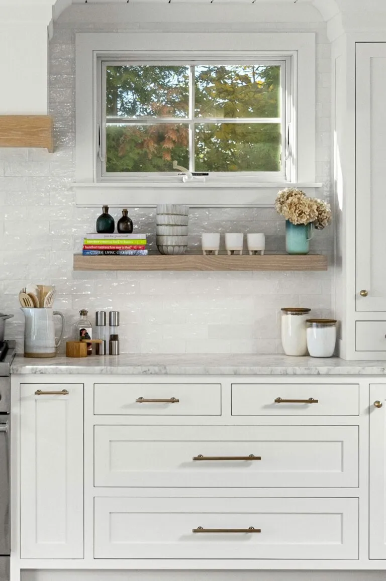 Light-filled kitchen featuring white cabinet colors, marble countertops, and brass hardware.