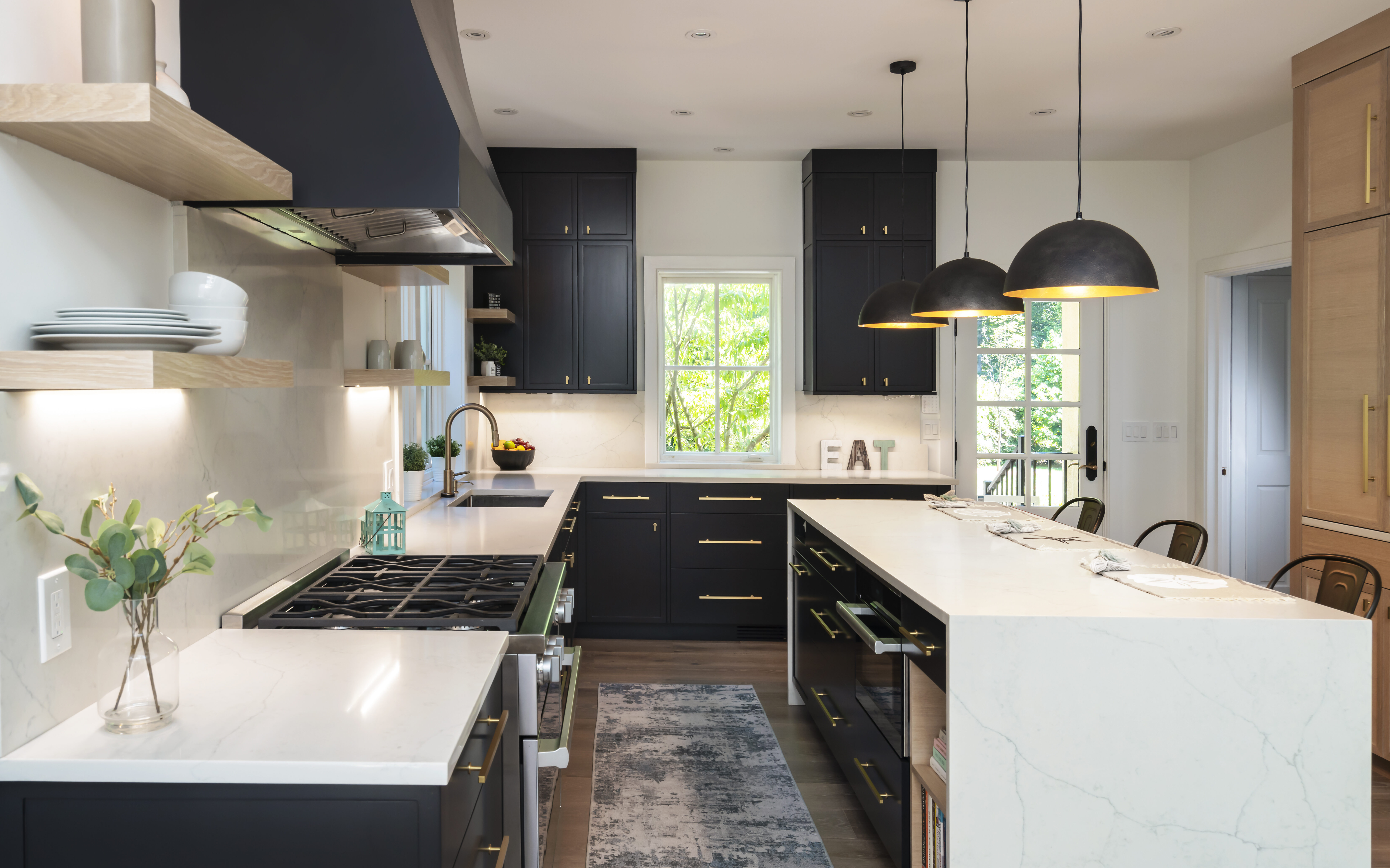 Sleek kitchen with black cabinets, white countertops, a central island, stainless steel appliances, and pendant lights.