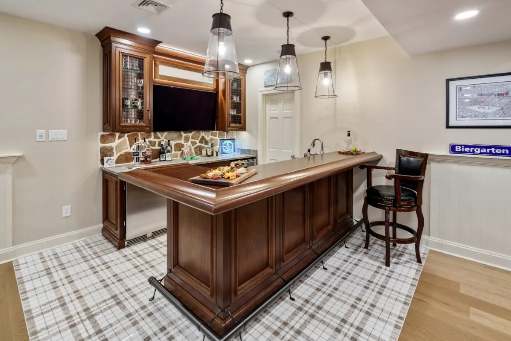 Elegant home bar with classic wooden cabinetry, stone backsplash, and modern pendant lighting.