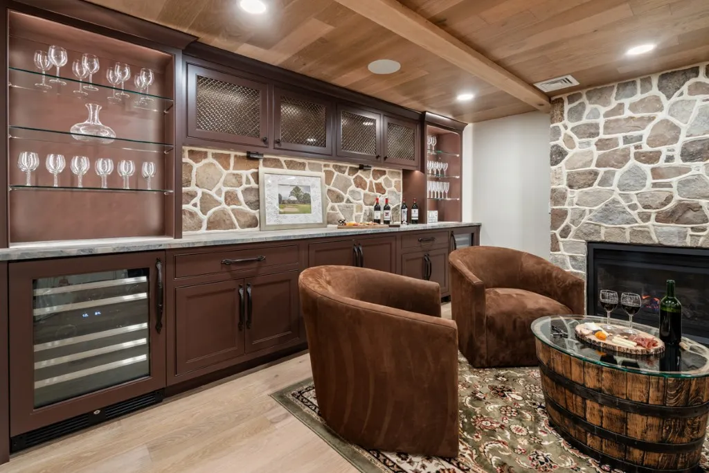Cozy home bar featuring a stone fireplace, plush seating, and rustic wine storage cabinets.