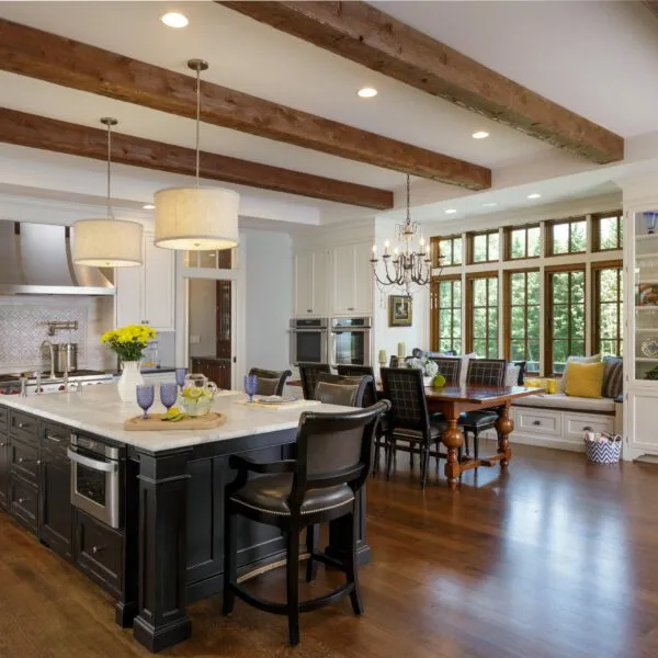 Elegant custom kitchen featuring white cabinetry, a large black island with marble countertops, and exposed wooden beams.