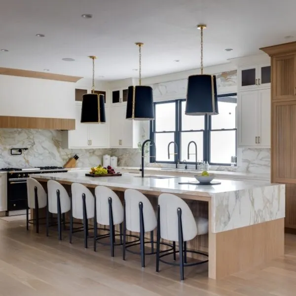 Modern luxury kitchen featuring a large marble island, black pendant lights, and a mix of white and wooden cabinetry.