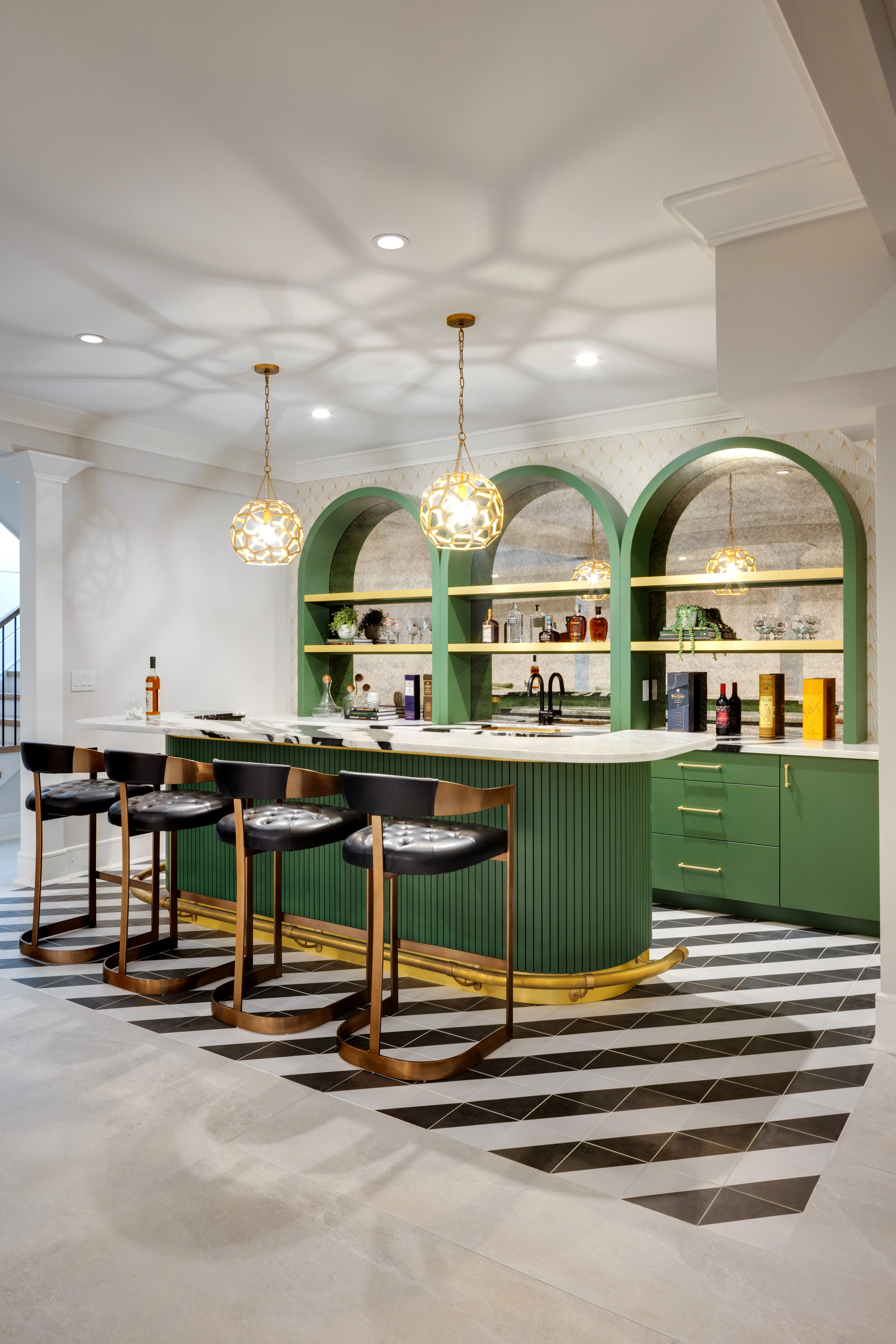 A modern home bar with green cabinetry, gold pendant lights, and stylish bar stools.