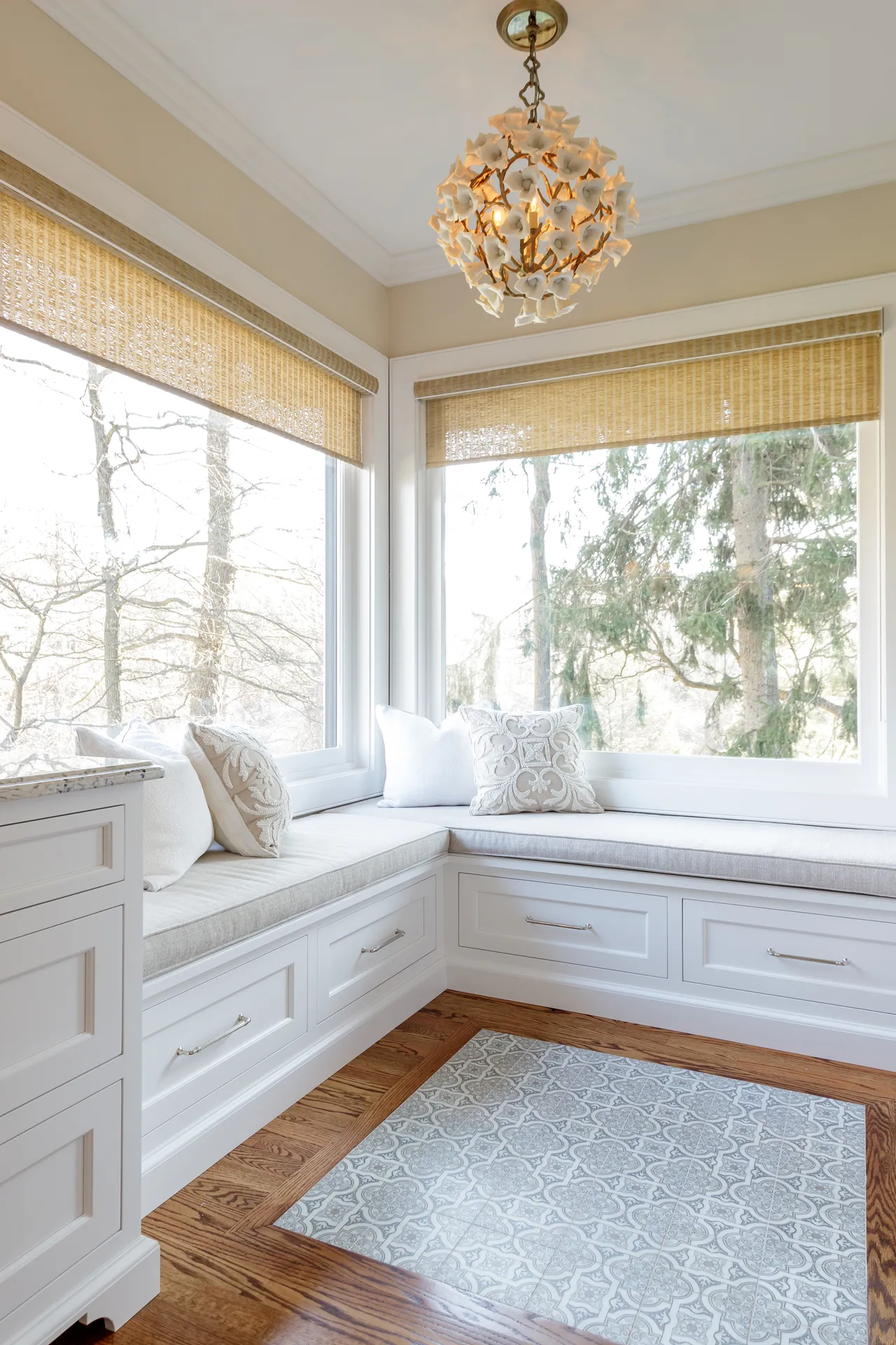 Bathroom corner with built-in white seating, large windows, decorative pillows, and an elegant light fixture.