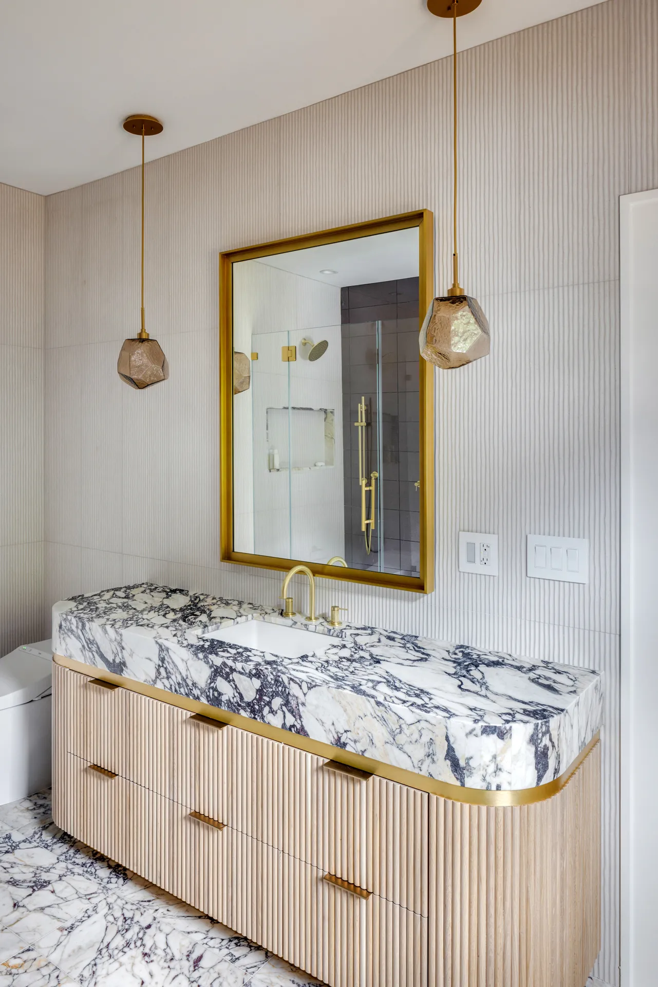 Bathroom featuring a marble vanity, gold fixtures, and elegant pendant lighting for a luxurious look.