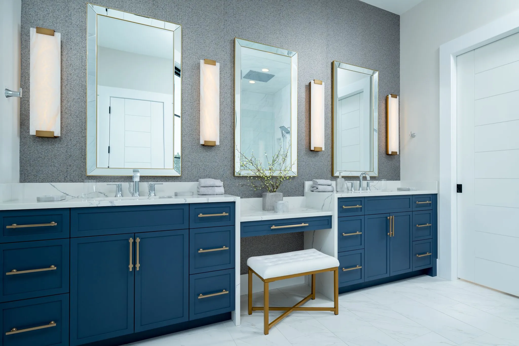 A refined bathroom displaying bespoke navy blue cabinets with gold accents, marble countertops, and elegant wall-mounted mirrors, showcasing premium custom cabinetry.