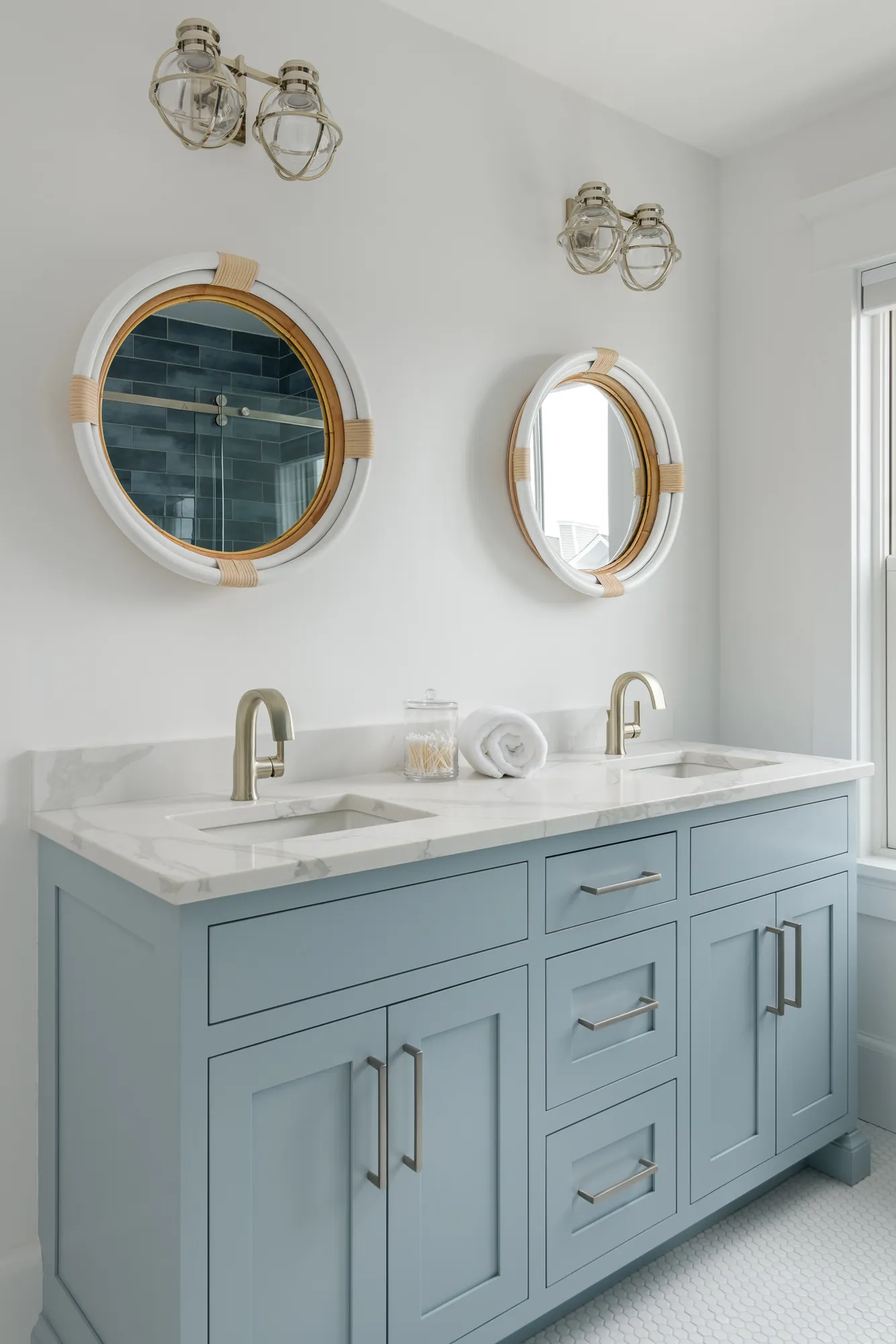 A modern coastal bathroom featuring a blue vanity with dual sinks, marble countertop, round mirrors, and nautical lighting fixtures.