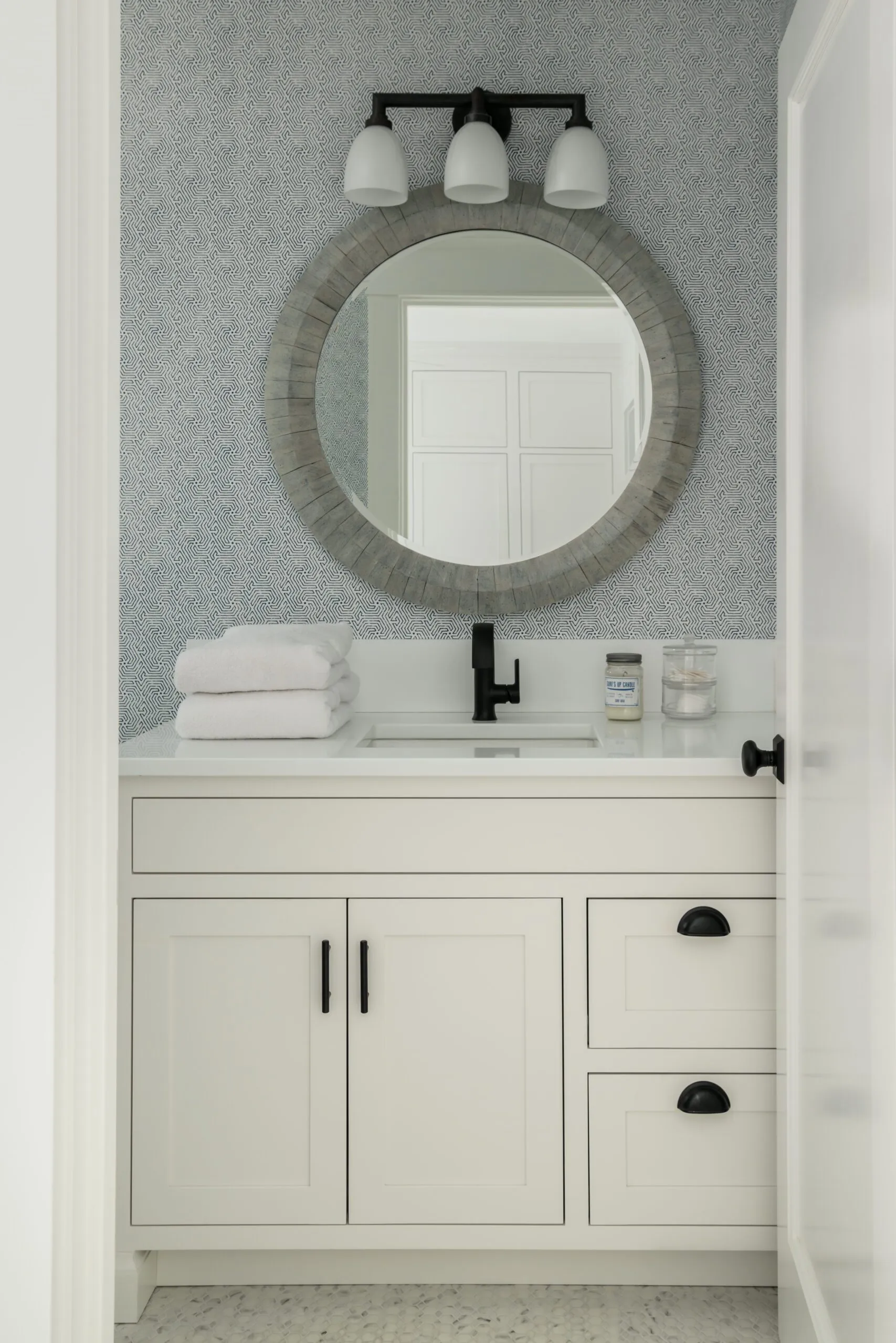 Modern bathroom featuring a white vanity with black hardware, round mirror, and stylish lighting.