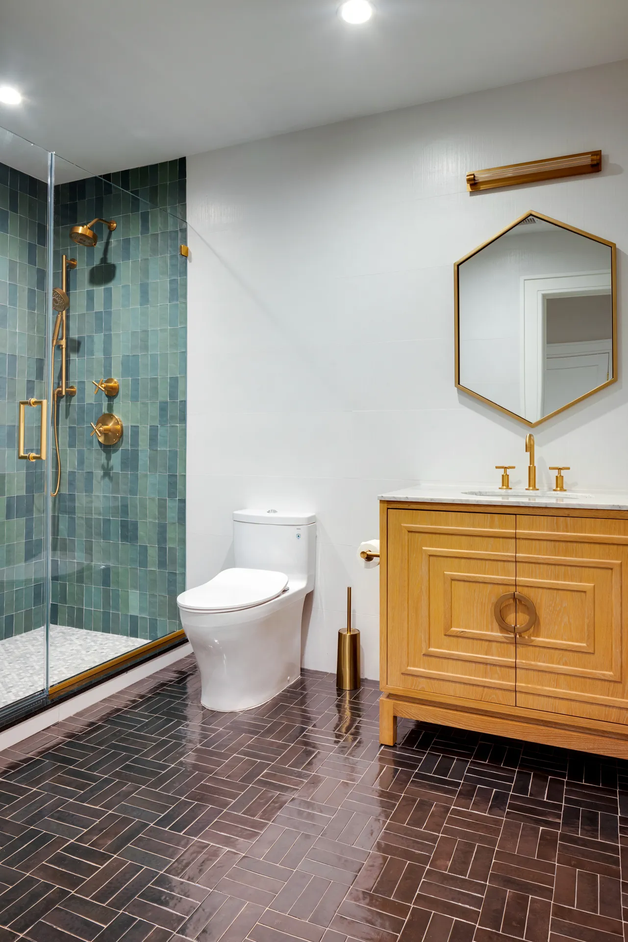Bathroom featuring a green tiled shower, gold fixtures, and a wooden vanity with a marble countertop.