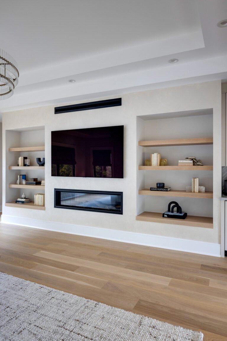 A modern living room wall featuring a fireplace, built-in TV, and minimalist floating shelves made of light-finished white oak, styled with decorative objects.