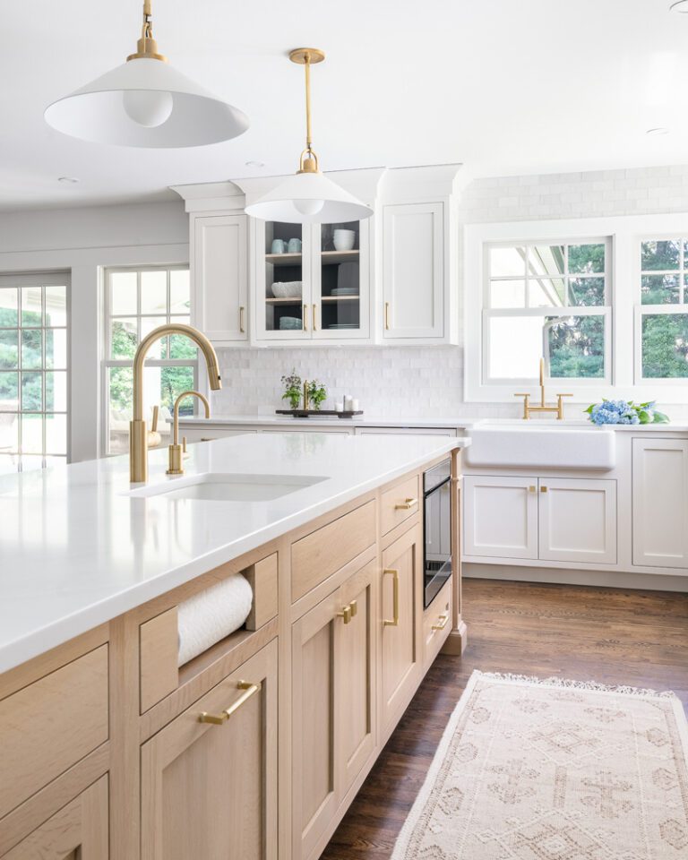 A modern transitional kitchen featuring a luxurious white oak island with brass hardware, complemented by white perimeter cabinets and a white subway tile backsplash.