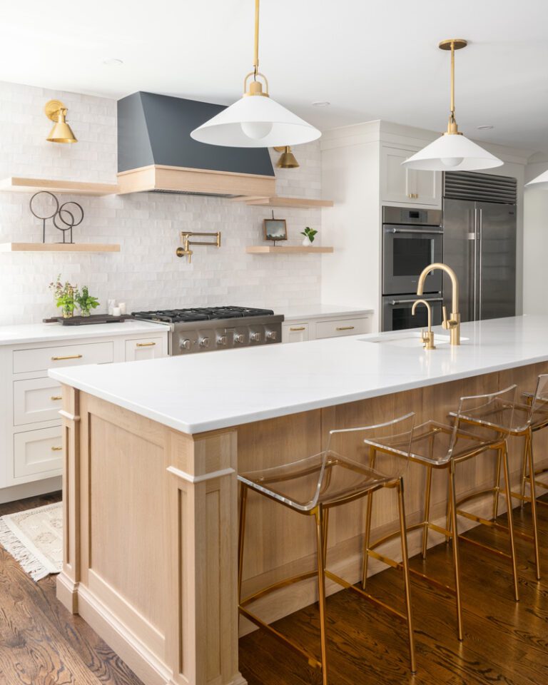 A transitional kitchen featuring luxury white oak island and floating shelves, white base cabinets, a dark range hood, stacked white subway tile backsplash, and brass accents.
