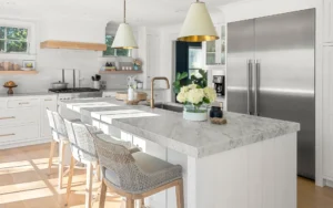 Modern farmhouse kitchen with marble countertops, island seating, stainless steel appliances, and decorative pendant lights.