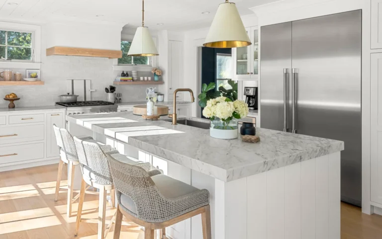 Modern farmhouse kitchen with marble countertops, island seating, stainless steel appliances, and decorative pendant lights.