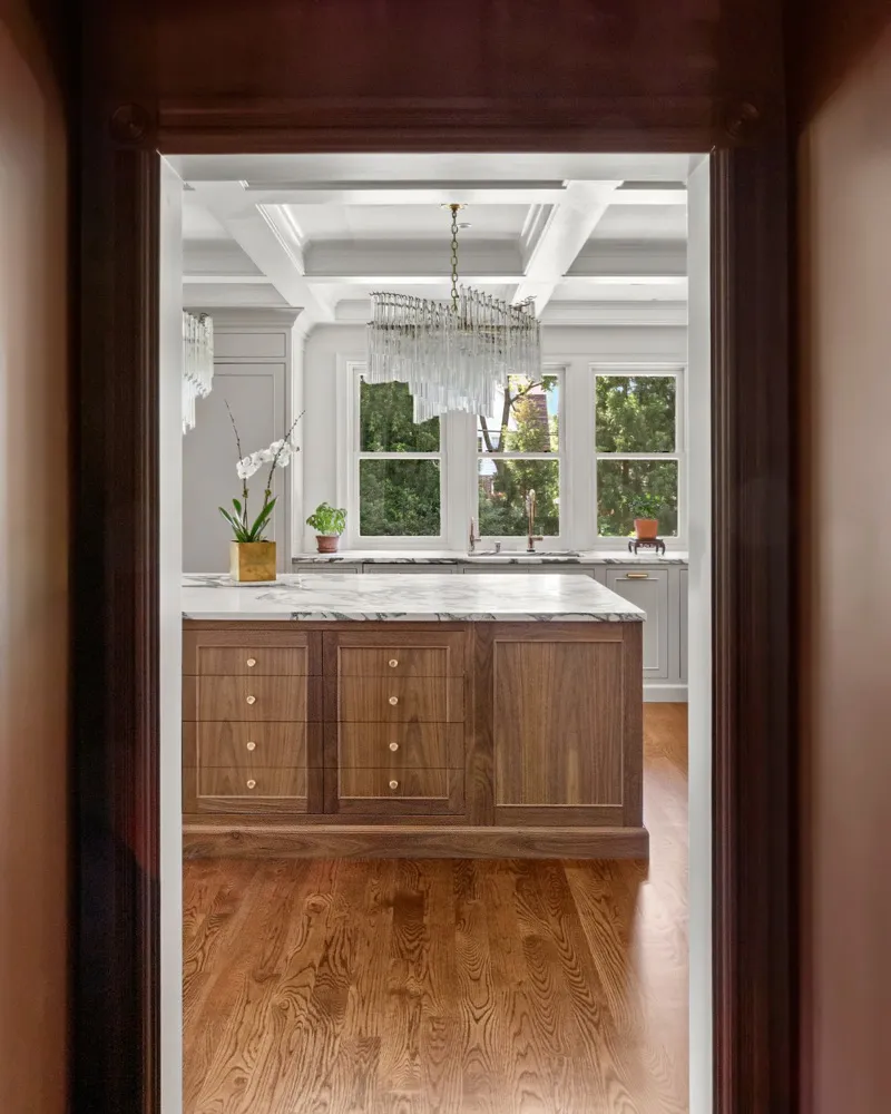 View into a quiet luxury kitchen featuring a dark wood island with master design cabinetry and a stunning chandelier