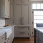 A custom greige kitchen appliance garage transforms from a closed, seamless pantry to a luxurious coffee station with an espresso machine when opened.
