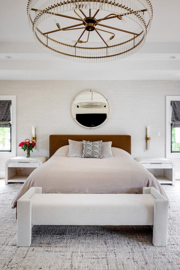 A wide and a detail shot of a luxurious Japandi bedroom featuring a large crystal chandelier, textured grasscloth wallpaper, a cognac-colored upholstered bed, and matching waterfall nightstands.